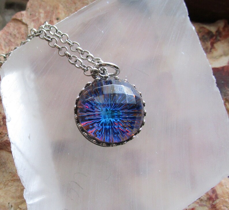 May include: A silver chain necklace with a round pendant featuring a blue and purple iridescent glass design with a silver bezel.
