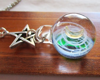 May include: A silver chain necklace with a five-pointed star charm and a glass orb pendant. The orb contains a crescent moon and swirling green and white lines.