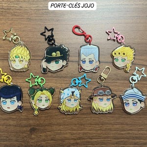 May include: A collection of nine acrylic keychains featuring stylised anime character heads with various expressions. Each charm includes a coloured metal star or lobster clasp attachment. The text PORTE-CLÉS JOJO is visible at the top centre.