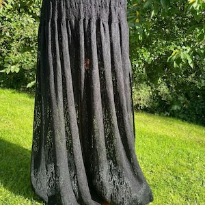 May include: A long, black, floor-length skirt made of a sheer, intricate lace fabric. The skirt features a gathered, elasticized waistband that creates a pleated effect, allowing the fabric to drape loosely and flow down to the hemline.