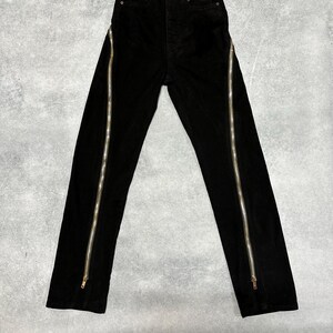 May include: Black corduroy pants with vertical silver zippers running along the outer seams. The pants have a classic five-pocket design and a button and zipper closure. The fabric appears to be a soft, textured corduroy.