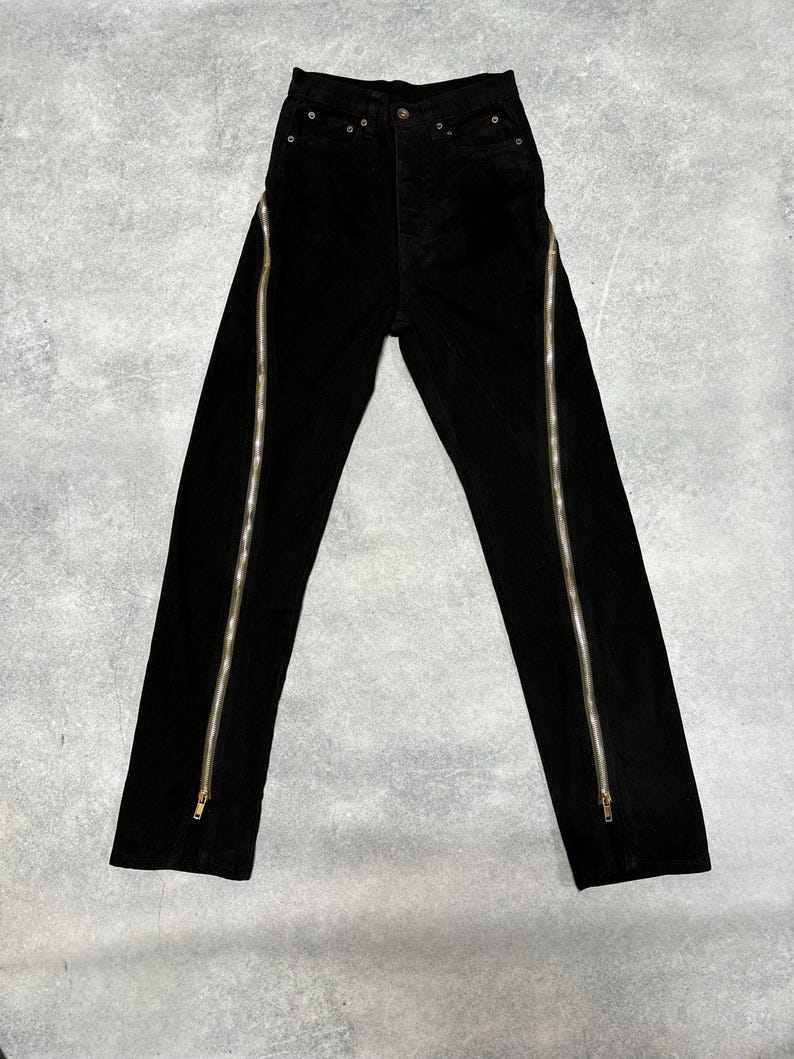 May include: Black corduroy pants with vertical silver zippers running along the outer seams. The pants have a classic five-pocket design and a button and zipper closure. The fabric appears to be a soft, textured corduroy.