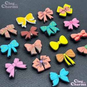 May include: A collection of 16 colourful bow-shaped shoe charms. The charms are made of rubber and feature various colours, patterns, and designs. The charms are perfect for adding a touch of personality to shoes.