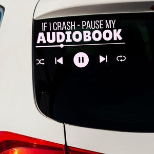 May include: White vinyl car decal with the text "IF I CRASH - PAUSE MY AUDIOBOOK" above a media player interface. The interface includes pause, rewind, fast forward, and shuffle icons. The decal is applied to a car window.