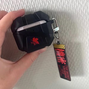 May include: Black protective case for wireless earbuds, with a red logo and a keychain tag with Japanese text and "TOP SECRET". The case is open, showing the white earbuds. The case is designed to protect the earbuds.