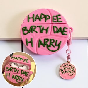 May include: Pink AirPod case with green text that reads "Happee Birth Dae Harry." The case has a matching charm attached. The case is designed to protect and personalize AirPods.