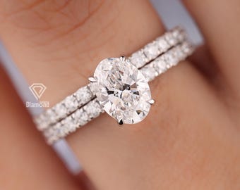 Set di anelli di fidanzamento con diamante ovale D VVS1 da 2 carati creato in laboratorio e alone nascosto, e set di fedi nuziali classiche con pavé delicato.