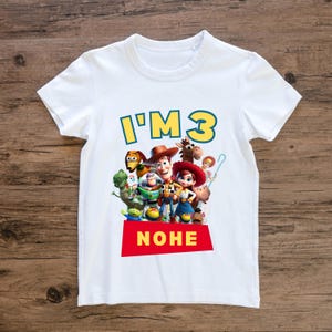 May include: White t-shirt featuring the phrase "I'M 3" in yellow and blue, with a red banner that says "NOHE". The shirt has a colorful graphic of characters from the Toy Story movie.