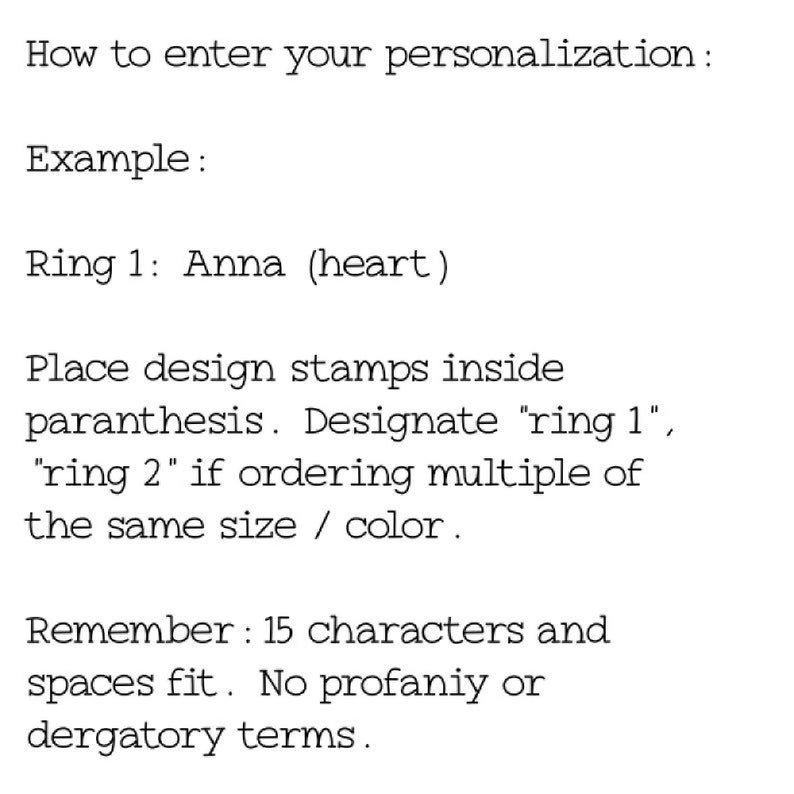 May include: Instructions on how to personalize a ring with a design stamp. The example shows "Ring 1: Anna (heart)". The text explains to place design stamps inside the parenthesis and to designate "ring 1" or "ring 2" if ordering multiple rings of the same size or color. It also states that only 15 characters and spaces fit and that no profanity or derogatory terms are allowed.