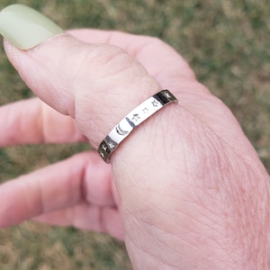 May include: A silver ring with a crescent moon and stars design. The ring is worn on a person's thumb.