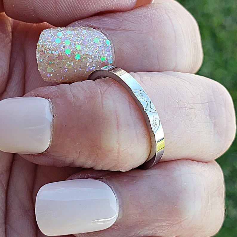 May include: A silver ring with a delicate floral design. The ring is worn on a finger with a light pink nail polish.