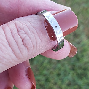 May include: A silver ring with the date "10.31" engraved on it. The ring is worn on a finger with brown nail polish.