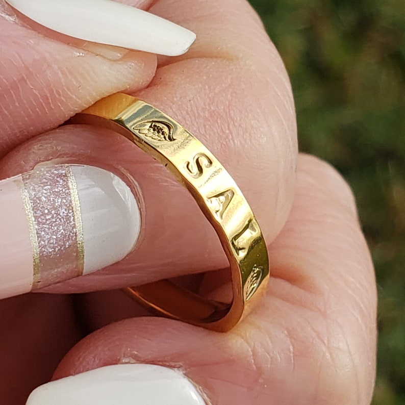 Puede incluir: Anillo de oro con la palabra "SAL" grabada en la banda. El anillo se lleva en un dedo.
