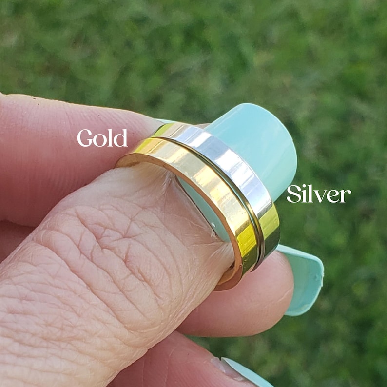 May include: Two flat-band rings, one with a metallic gold finish and one with a metallic silver finish, are stacked together. The word Gold is printed in white text near the gold ring, and the word Silver is printed in white text near the silver ring.