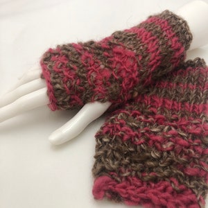 May include: A pair of fingerless gloves knitted in a brown and pink striped pattern. The gloves are made with a soft, fuzzy yarn.