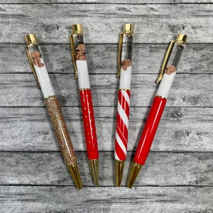 May include: Four clear pens with gold accents and red, white, and gold designs. The pens have a clear section that contains small brown objects.