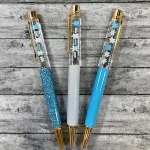 May include: Three clear pens with gold accents and snowflake designs. The pens have different colored glitter: blue, white, and light blue.