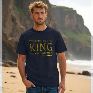 Puede incluir: Camiseta azul marino con texto dorado que dice: "YOU COME AT THE KING, YOU BEST NOT MISS." La cita es de Omar de The Wire. La camiseta es de estilo cuello redondo.
