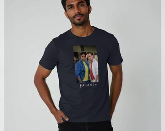 May include: Navy blue t-shirt featuring a rectangular image of two men, one in a blue jacket and the other in a white coat. The word "FRIENDS" is printed in white below the image. The shirt is a classic crew neck style.