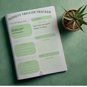 Könnte beinhalten: Notizbuch zur Verfolgung von Angstauslösern mit grünen Akzenten. Das Notizbuch enthält Abschnitte für Datum, Uhrzeit, Grund und Symptome. Der Text auf der Seite lautet "DATE 15TH MARCH 2026" und "TIME 8.30PM". Eine kleine Topfpflanze befindet sich im Hintergrund.