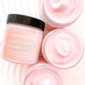 May include: Three jars of pink body lotion with a label that reads "sweet clementine soaps cocoa butter cashmere body lotion net wt 5 oz | 141g"