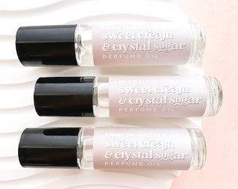 May include: Three glass roller bottles with black caps and labels that read "sweet cream & crystal sugar perfume oil". The labels are a gradient of pink and white.