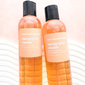 May include: Two bottles of body wash and bubble bath with orange liquid and black caps. The labels read "Sweet Clementine Soaps" and "Clementine Clouds". Each bottle contains 8 fl oz (236 mL).