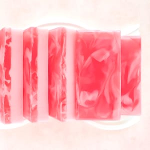 May include: Five rectangular bars of soap arranged in a row. Each bar features a marbled pattern with shades of bright pink and soft pale pink. The soap bars have a smooth, semi-translucent finish with distinct swirls of color throughout the surface.