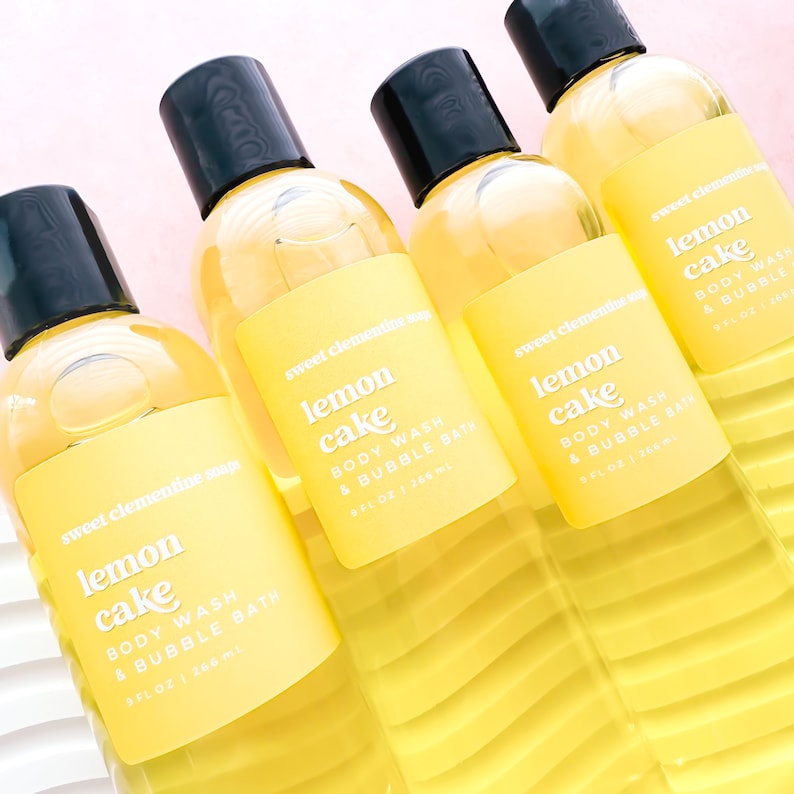May include: Four yellow bottles of sweet clementine soap with black caps. Each bottle has a label that reads "lemon cake body wash & bubble bath 8 fl oz | 266 ml".