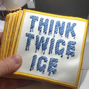 May include: A stack of square patches with the text "THINK TWICE ICE" embroidered in blue on a white background. Each patch has a yellow border.