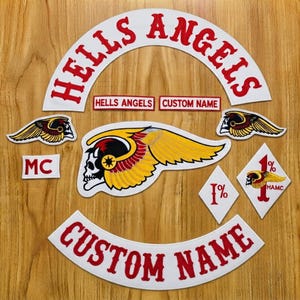 Puede incluir: Una colección de parches bordados que incluye un parche blanco arqueado grande con texto rojo que dice HELLS ANGELS, un emblema central de calavera alada, dos parches de calavera alada más pequeños, un parche de diamante 1% y dos parches curvos con nombres personalizados.