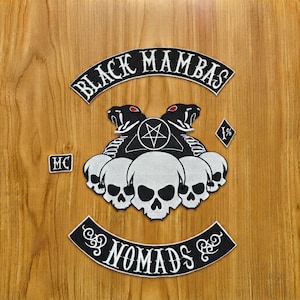 Puede incluir: Un conjunto de parches bordados que incluye un arco superior negro con el texto BLACK MAMBAS, un emblema central de dos serpientes con ojos rojos y un pentagrama sobre tres calaveras, un parche pequeño MC, un parche de diamante 1% y un arco inferior con NOMADS.