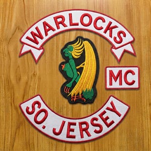 May include: A set of embroidered patches featuring a top rocker with the text WARLOCKS, a bottom rocker with the text SO. JERSEY, a rectangular patch with the text MC, and a central patch depicting a green figure with yellow hair.