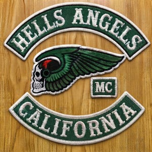 May include: A set of embroidered patches featuring a top rocker with the text HELLS ANGELS, a bottom rocker with the text CALIFORNIA, a central winged skull emblem with green and black details, and a small rectangular patch with the letters MC.