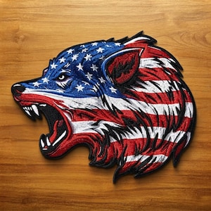 May include: An embroidered patch shaped like a wolf head in profile with its mouth open, revealing sharp teeth. The wolf features a pattern of the American flag, with white stars on a blue background on the snout and red and white stripes on the neck.