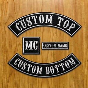 Puede incluir: Un conjunto de cuatro parches bordados negros con bordes y letras blancas. El parche en arco superior dice CUSTOM TOP, el inferior CUSTOM BOTTOM, un parche cuadrado presenta las letras MC y un parche rectangular dice CUSTOM NAME.