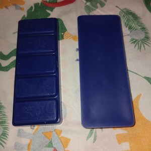 Könnte beinhalten: Zwei blaue rechteckige Wachsplatten, eine mit fünf Abschnitten und die andere durchgehend. Die Platten liegen auf einem bunten Stoffhintergrund.