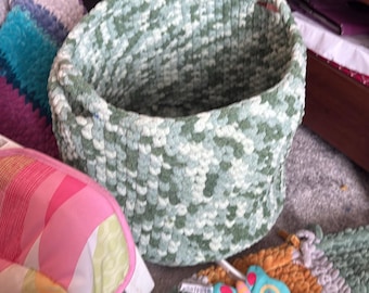May include: A green and white woven storage basket with a round shape. The basket is made of a soft, textured material and has a wide opening.