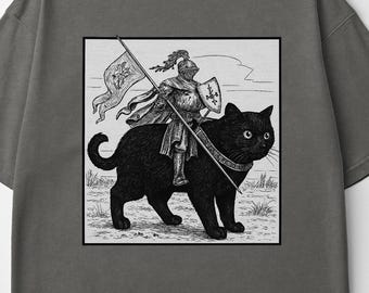 May include: Dark grey t-shirt featuring a black and white illustration of a knight riding a black cat, holding a flag and shield. The shirt has a crew neck and short sleeves. The text "COMFORT COLORS" is printed on the collar.