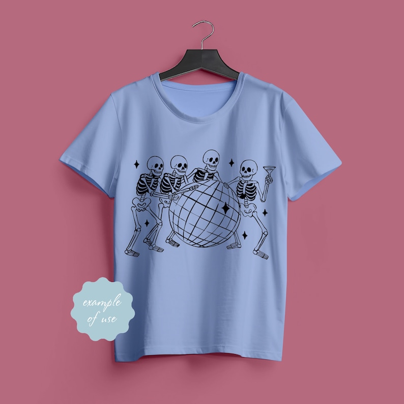May include: Light blue t-shirt featuring a black graphic of skeletons surrounding a disco ball. The design includes four skeletons, each with a different pose, and a few diamond-shaped accents. The shirt is hanging on a black hanger.
