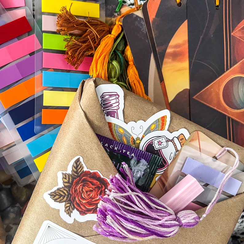 May include: A brown paper envelope with a purple tassel, a butterfly sticker, and a rose sticker. The envelope is filled with colorful bookmarks and a card with the text "Black Tea".