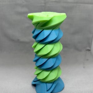 May include: A two-tone, abstract sculpture in shades of blue and green. The object has a spiraling design, with alternating layers of light blue and lime green, creating a visually dynamic and modern aesthetic. The sculpture is a unique decorative piece.