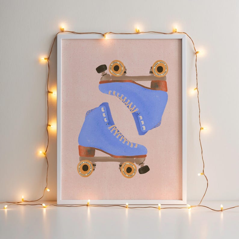 May include: A framed print featuring a pair of blue roller skates with tan wheels and laces. The skates are set against a pink background. The white frame is decorated with a string of small, warm-toned lights.