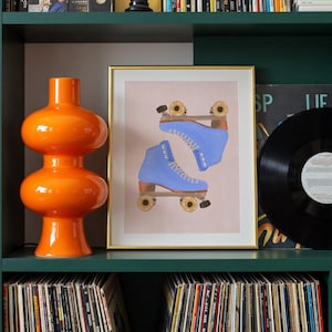 May include: An orange glass lamp with a rounded shape sits on a green shelf next to a framed print of blue roller skates. A black vinyl record is also on the shelf, with a collection of records below.