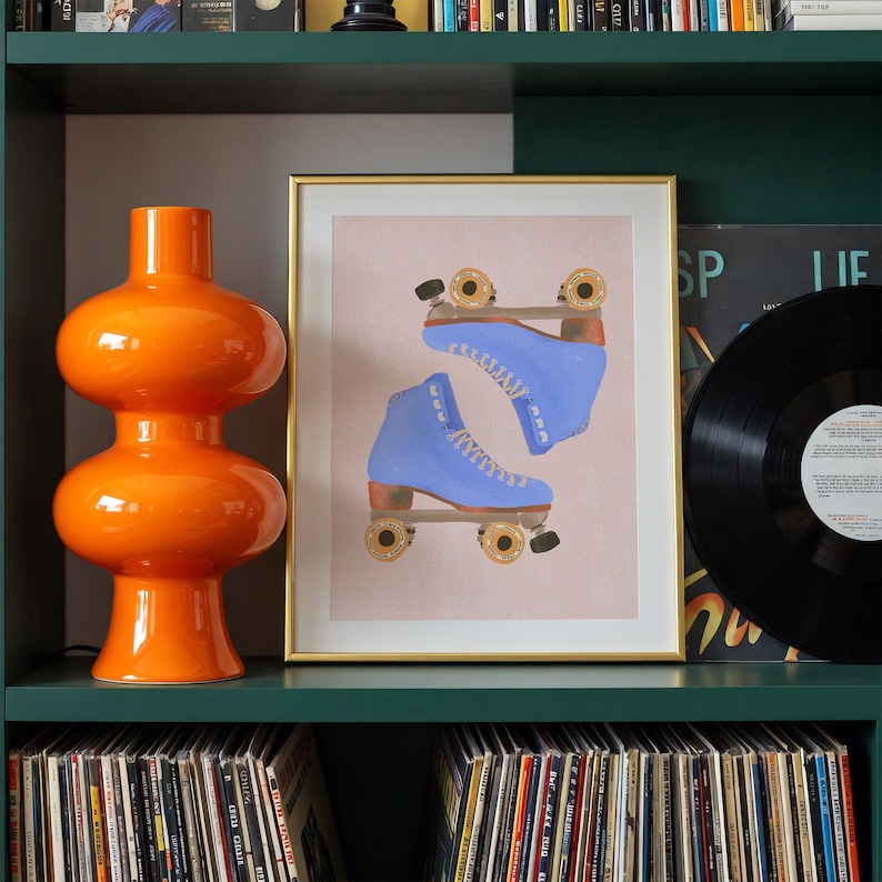 May include: An orange glass lamp with a rounded shape sits on a green shelf next to a framed print of blue roller skates. A black vinyl record is also on the shelf, with a collection of records below.