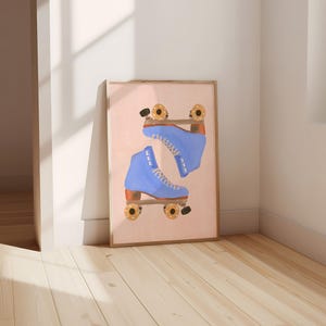May include: A framed print featuring a pair of blue roller skates. The skates are depicted in a watercolor style against a light pink background. The wheels are gold and black, and the boots are laced with white laces. The frame is a light brown color.