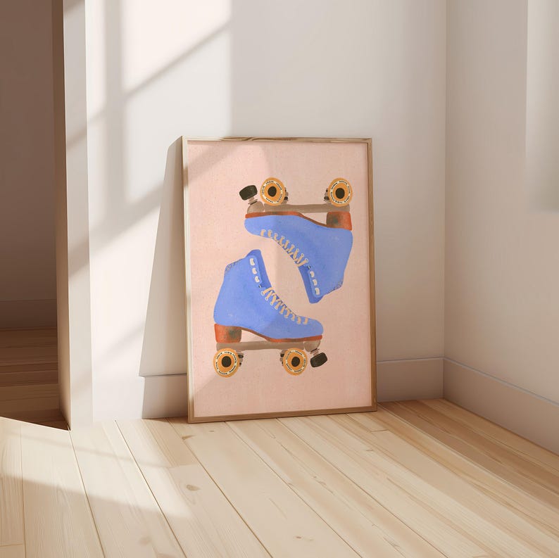 May include: A framed print featuring a pair of blue roller skates. The skates are depicted in a watercolor style against a light pink background. The wheels are gold and black, and the boots are laced with white laces. The frame is a light brown color.