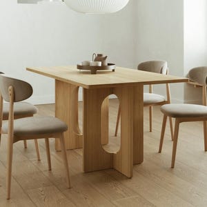 Può includere: Un tavolo da pranzo in rovere chiaro con piano rettangolare e base dal design unico con intagli curvi. Quattro sedie abbinate con sedute imbottite beige chiaro e telai in legno circondano il tavolo. Un vassoio con teiera e tazze è appoggiato sul tavolo.