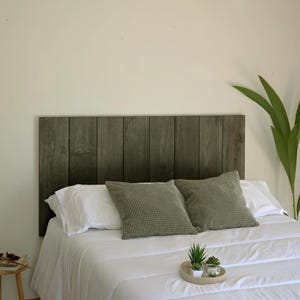 Puede incluir: Un cabecero de madera gris con tablones verticales se coloca sobre una cama con ropa de cama blanca. Dos almohadas verdes estampadas descansan contra el cabecero. Una pequeña bandeja con plantas está sobre la cama.