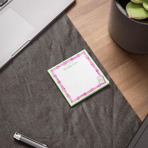 May include: A square notepad with a light green border and a pink bamboo-style frame. The notepad has the text "GET YOUR MAHJ ON!" and a small Chinese character in the corner. The notepad is on a dark gray surface.